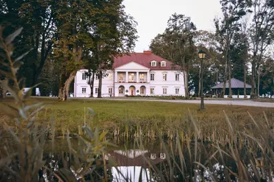 a white house with a red roof reflected in a pond at Bistrampolis Manor in Kučiai