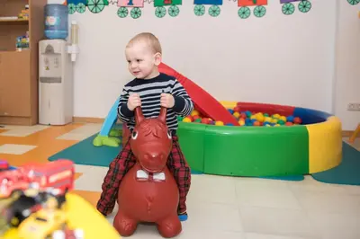 a baby standing on a toy horse in a play room at Grand SPA Lietuva Hotel Druskininkai in Druskininkai