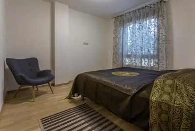 a bedroom with a bed and a chair and a window at Violetos Lux Apartamentai in Druskininkai