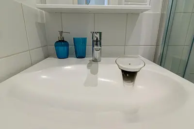 a white bathroom with a sink and two blue glasses at Sky Studio near the Vilnius Center in Vilnius
