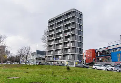 a tall building with cars parked in a parking lot at Sky Studio near the Vilnius Center in Vilnius