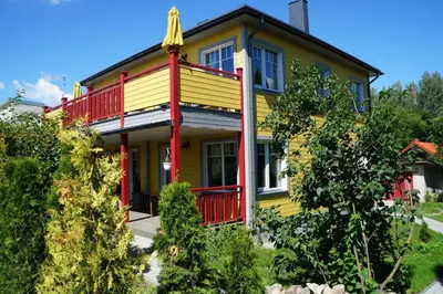 a yellow and red house with a red balcony at Guest House Mr Fox in Druskininkai