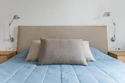 a bed with a blue comforter and two lamps at Aura apartamentai in Druskininkai