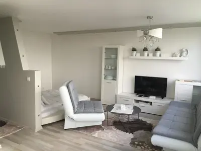 a white living room with a chair and a tv at Angel's Dream Apartment in Anykščiai