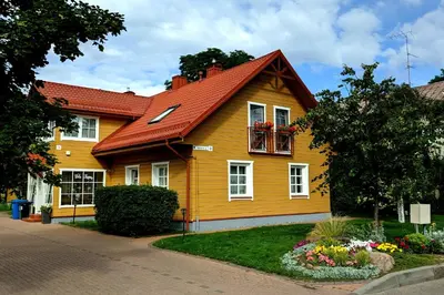 a yellow house with a red roof and flowers at Vila Liepa in Birštonas