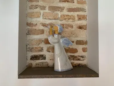 a ceramic angel statue sitting on a shelf next to a brick wall at Very Vilnius Pilies street in Vilnius