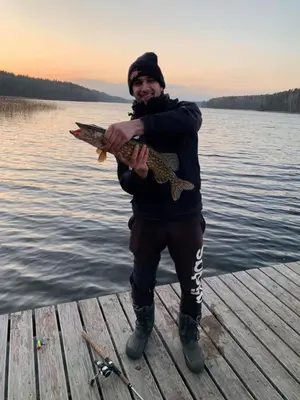 a man standing on a dock holding a fish at Kaimo Turizmo Sodyba Šniūrai in Mindūnai