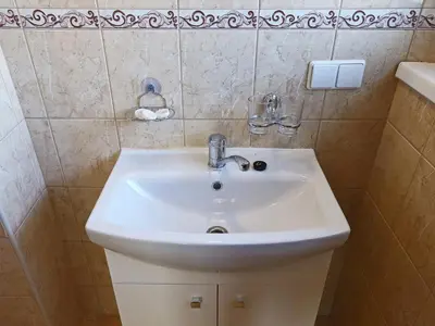 a bathroom with a white sink and a tiled wall at Juro Guest House in Šiauliai
