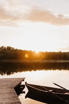 a boat sitting on the water next to a dock at Beržų namelis - Birch cabin in Kučiūnai