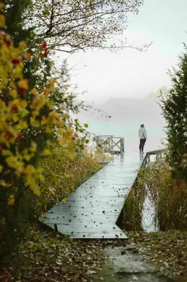 a person walking on a wooden bridge over the water at Beržų namelis - Birch cabin in Kučiūnai
