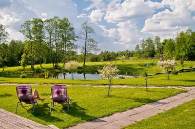 two chairs sitting in the grass near a pond at Adomo Sodyba in Dubingiai