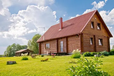 a wooden barn with a red roof in a field at Adomo Sodyba in Dubingiai
