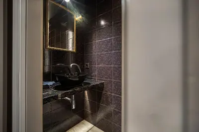 a black tiled bathroom with a sink and a mirror at Secret Lounge - Cozy Studio with Sauna and Jacuzzi in Vilnius