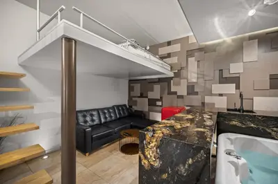a living room with a black leather couch and a staircase at Secret Lounge - Cozy Studio with Sauna and Jacuzzi in Vilnius
