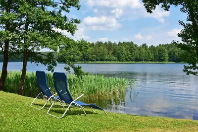 two chairs sitting on the grass near a lake at Mekų slėnis in Degučiai