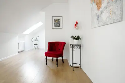 a red chair in a white room with a table at Baron's Arthouse Apartment in Vilnius