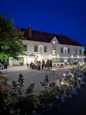 a large white building with people sitting outside at night at Central Hotel Radviliškis in Radviliškis
