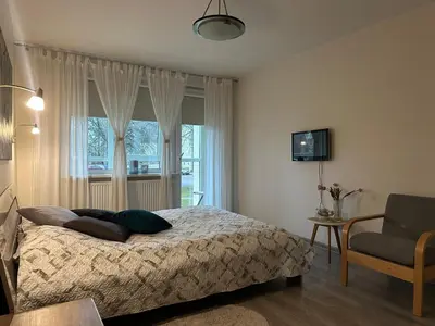 a bedroom with a bed and a chair and a window at Smiltės apartamentai in Birštonas