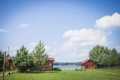 a couple of buildings in a field with a body of water at Pušynėlis in Miežonys