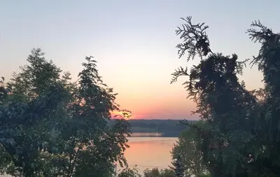 a sunset over a lake with trees in the foreground at Vijuandra in Zarasai