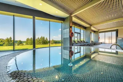 an indoor swimming pool in a house with glass windows at Vilnius Grand Resort in Ežeraičiai