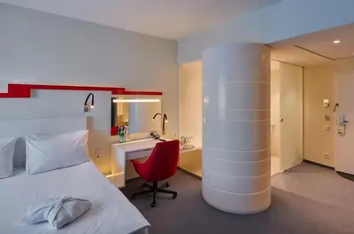 a hotel room with a bed and a red chair and a desk at Holiday Inn Vilnius by IHG in Vilnius
