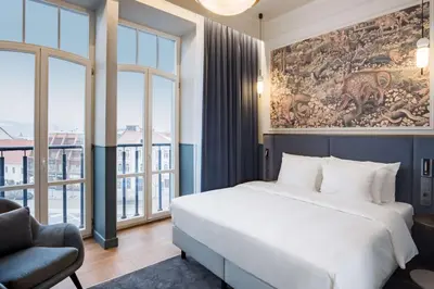 a bedroom with a bed and a chair and windows at Radisson Collection Astorija Hotel, Vilnius in Vilnius