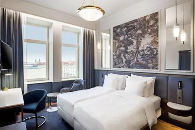a hotel room with a bed and a desk and two windows at Radisson Collection Astorija Hotel, Vilnius in Vilnius