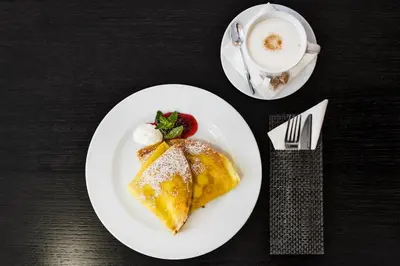 a white plate with a piece of cake and a cup of coffee at Amberton Cozy Hotel Kaunas in Kaunas