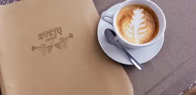 a cup of coffee sitting on a table next to a notebook at Žvejų užeiga in Šiauliai