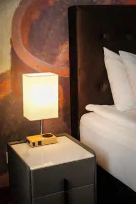 a lamp on a night stand next to a bed at Agneta Apartamentai in Druskininkai