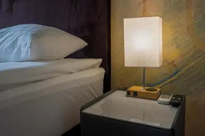 a lamp on a night stand next to a bed at Agneta Apartamentai in Druskininkai