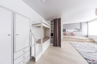 a white kitchen with a staircase and a living room at Sandra apartamentai in Kaunas