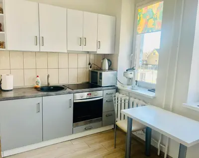a kitchen with white cabinets and a sink and a table at Ezero apartamentai in Šiauliai
