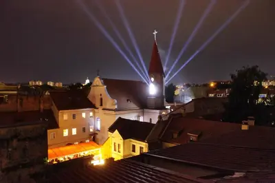 a church with a steeple and a clock tower at night at Vokiečių g. in Vilnius