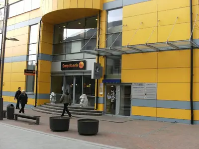 a yellow building with people walking in front of it at Litrada Apartments in Šiauliai