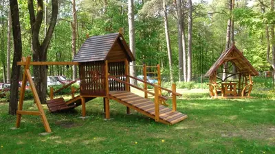 two wooden playground equipment in a park with trees at Hotel Dainava in Druskininkai