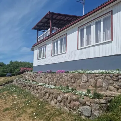 a house with a stone retaining wall and flowers at Griežto 5 in Zarasai