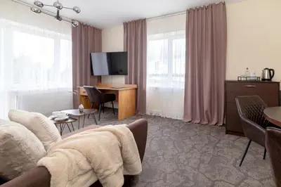 a hotel room with a couch and a desk with a television at Butenas Hotel Tyla in Biržai