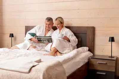 a man and woman sitting on a bed reading a magazine at Butenas Hotel Tyla in Biržai