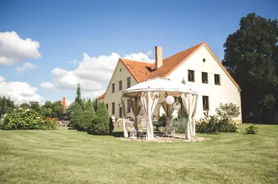 a white house with an umbrella and chairs in the yard at Akmenių Dvaras in Akmeniai