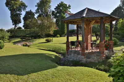 a gazebo in a garden with a stone wall at Ašmonienės svečių namai 