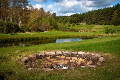 a pond in the middle of a grassy field with a fence at Sodyba Dubinga in Molėtai