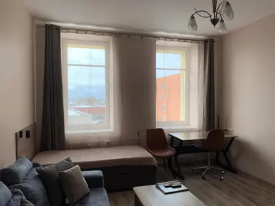a living room with a bed and a desk and two windows at Sweet Apartments in Šiauliai