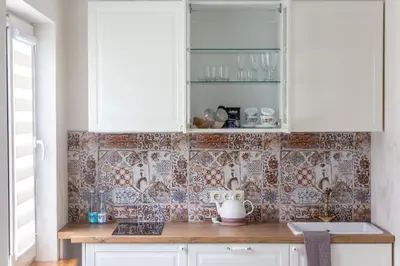 a kitchen with white cabinets and tiles on the wall at Classic Old Town Apartment in Druskininkai