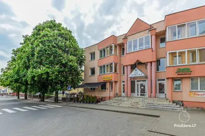 a building on the side of a street with a tree at Guest House Simona in Lazdijai