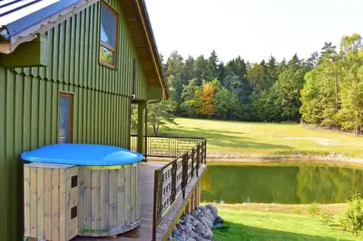 a house with a hot tub on a deck next to a pond at Vip Forest dreams villa in Anykščiai