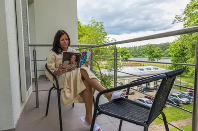 a woman sitting on a balcony reading a book at Sanatorija ,,Tulpės