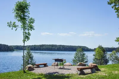 a picnic table and benches on the shore of a lake at Mekų vila in Degučiai