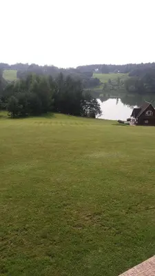a large green field with a house and a lake at Country Houses Vidų Sodyba in Utena